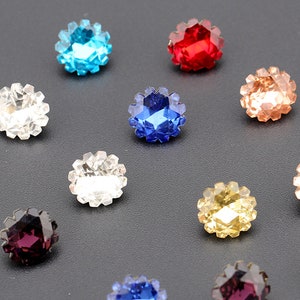 May include: Assortment of colorful, faceted, round, glass rhinestones with a starburst design. The rhinestones are arranged on a black surface.