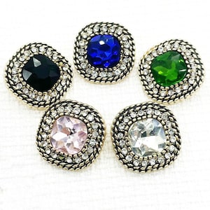 May include: Five square-shaped buttons with gold-toned metal frames and clear rhinestone accents. Each button features a different coloured glass gem in the centre: black, blue, green, pink, and clear.