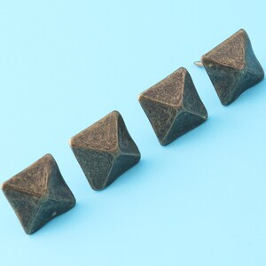 Könnte beinhalten: Vier antike goldfarbene pyramidenförmige Nieten auf hellblauem Hintergrund.