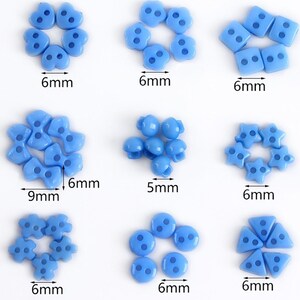 Könnte beinhalten: Sortiment an hellblauen Kunststoffknöpfen in verschiedenen Formen, darunter Herzen, Sterne, Kreise und Quadrate. Die Knöpfe haben jeweils zwei Löcher und sind zwischen 5 mm und 9 mm groß.