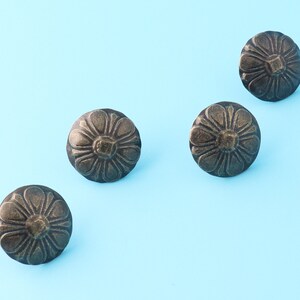 Könnte beinhalten: Vier antike, goldfarbene, dekorative Metall-Nägel mit floralem Muster. Die Nägel sind diagonal auf einem hellblauen Hintergrund angeordnet.