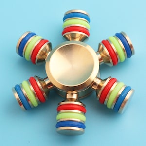 May include: A gold metal fidget spinner with six colorful rings. The rings are red, blue, green, and yellow.