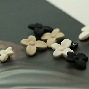 Puede incluir: Surtido de botones con forma de flor en beige, blanco y negro.