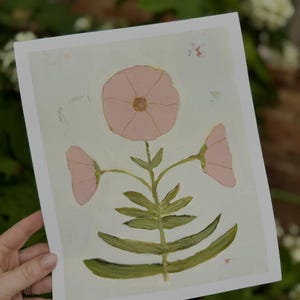 May include: An art print showcasing a stylized flower with three pink blooms and green foliage. The artwork is set against a pale blue backdrop with visible brushstrokes, giving it a gentle, artistic feel.