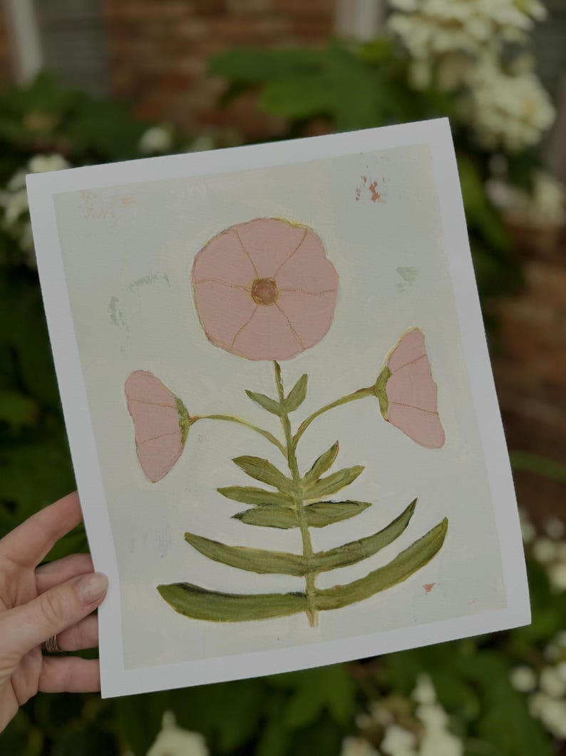 May include: An art print showcasing a stylized flower with three pink blooms and green foliage. The artwork is set against a pale blue backdrop with visible brushstrokes, giving it a gentle, artistic feel.
