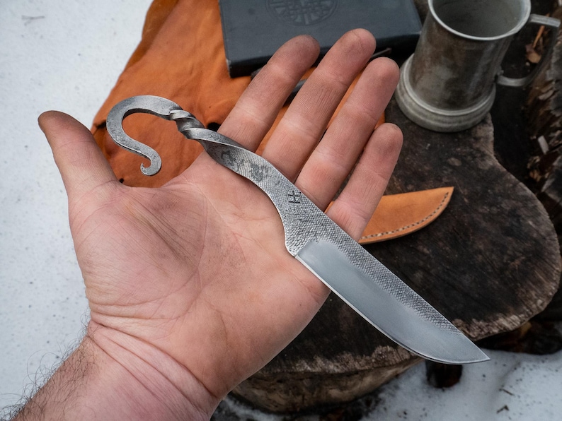 Pu&ograve; includere: Coltello in acciaio forgiato a mano con manico curvo e lama strutturata. Il coltello presenta un design a spirale sul manico e una punta affilata. La lama ha un motivo strutturato e la lettera "H" &egrave; stampata sulla lama.
