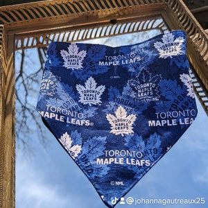 May include: A blue and white bandana featuring the Toronto Maple Leafs logo repeated throughout. The bandana is hanging from a gold mirror frame. The text "TORONTO MAPLE LEAFS" is visible on the bandana.