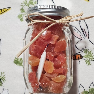 May include: A glass jar filled with dried fruit, including papaya, mango, and pineapple. The jar has a silver lid and is tied with a brown ribbon. The label on the jar reads "Made in the USA".