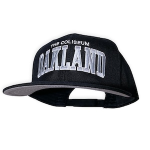 May include: Black and grey baseball cap with the text "THE COLISEUM OAKLAND" embroidered on the front.