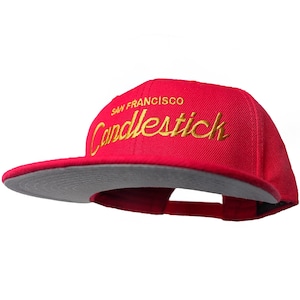 May include: A red baseball cap with a gray brim. The cap has gold embroidery that reads "San Francisco Candlestick".