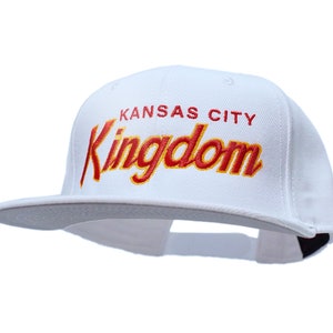 Könnte beinhalten: Weiße Baseballkappe mit einem roten und gelben gestickten Logo, auf dem "Kansas City Kingdom" steht.