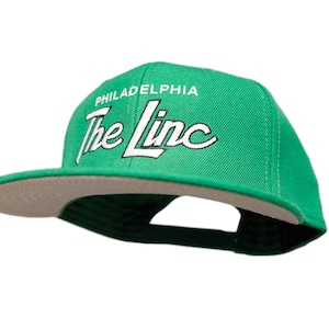 May include: A green and grey baseball cap with the text "PHILADELPHIA The Linc" embroidered in white.