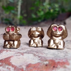 Könnte beinhalten: Drei goldene Affenfiguren, jede mit roten Augen, die das Sprichwort "Sehe kein Übel, höre kein Übel, sprich kein Übel" darstellen.