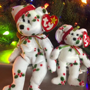 May include: Two white plush beanie baby bears with red and green holly patterns. The larger bear is wearing a red and white Santa hat. Both bears have a Ty tag attached.