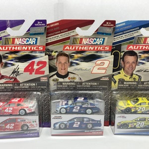 May include: Three NASCAR Authentic's die-cast cars in their packaging. The cars are Kyle Larson #42, Brad Keselowski #2, and Matt Kenseth #20. The cars are red, blue, and yellow, respectively. The packaging is purple, blue, and light blue, respectively.