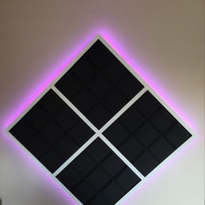 May include: A diamond-shaped sound panel with a white frame and black acoustic foam tiles. The panel is illuminated with pink LED lights around the perimeter.