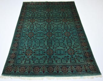 May include: A rectangular area rug featuring a deep teal background with a repeating geometric pattern in black and dark red. The design includes central floral-like motifs and a wide border with intricate repeating shapes and white fringe ends.