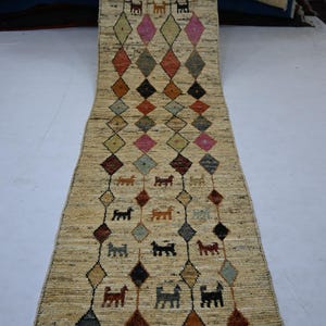 Puede incluir: Una alfombra de pasillo larga y estrecha con una base de color crema que presenta un patrón repetitivo de contornos de diamantes oscuros. Dentro de los diamantes hay pequeñas figuras de animales multicolores y formas de diamantes sólidos.