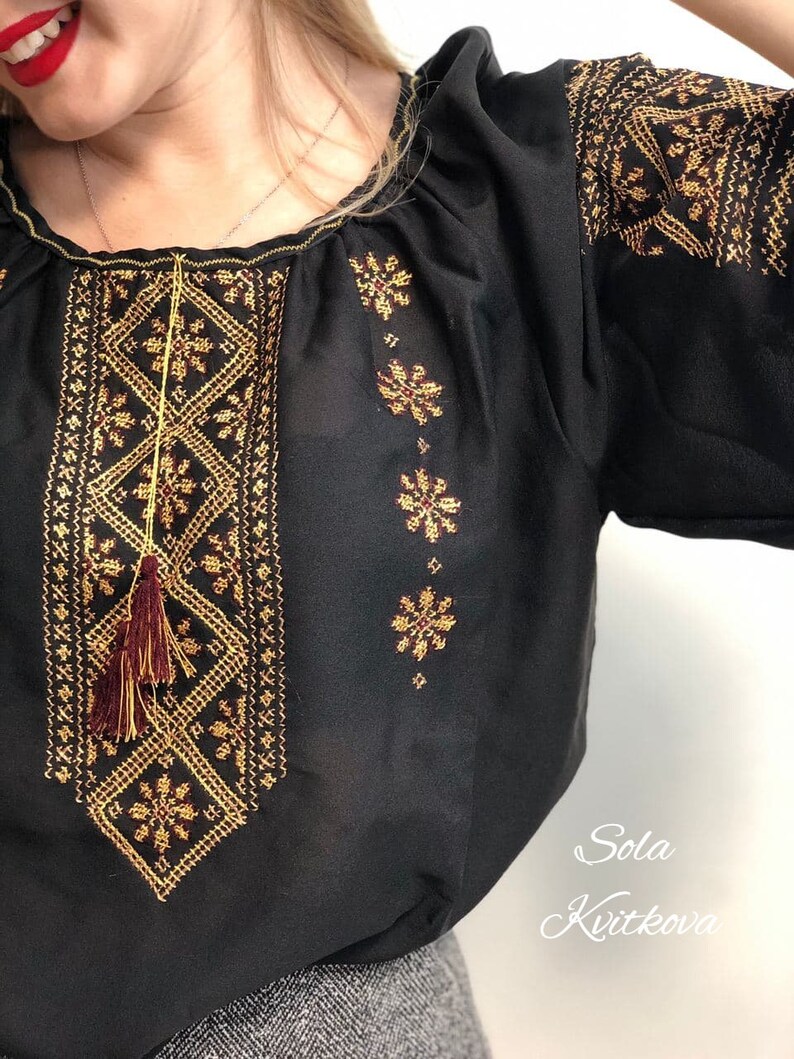 Pu&ograve; includere: Blusa nera in chiffon con ricami dorati e bordeaux. Il ricamo presenta motivi geometrici e nappe. La blusa ha un collo rotondo e maniche corte.