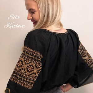 Pu&ograve; includere: Una blusa nera con ricami dorati sulle maniche. I ricami presentano motivi geometrici. La blusa ha un collo rotondo e una vestibilit&agrave; ampia.