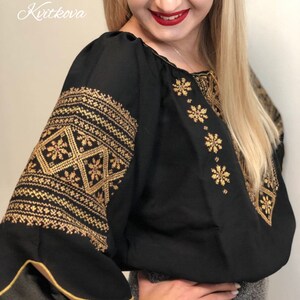 Pu&ograve; includere: Una blusa nera con ricami dorati. Il ricamo presenta un motivo geometrico e motivi floreali. La blusa ha un collo a volant e maniche lunghe.