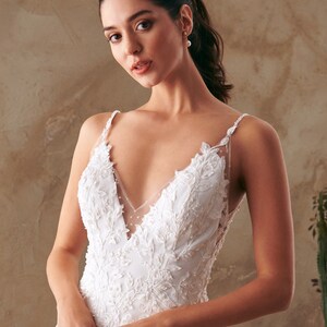 K&ouml;nnte beinhalten: Ein wei&szlig;es Brautkleid mit einem Spitzenoberteil und einem R&uuml;schenrock. Das Kleid hat einen V-Ausschnitt und d&uuml;nne Tr&auml;ger.
