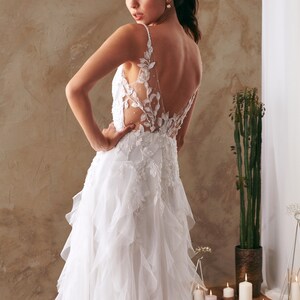 K&ouml;nnte beinhalten: Ein wei&szlig;es Brautkleid mit einem Spitzenoberteil und einem flie&szlig;enden T&uuml;llrock. Das Kleid hat einen tiefen R&uuml;cken und zarte florale Stickereien.