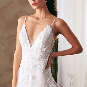 K&ouml;nnte beinhalten: Ein wei&szlig;es Brautkleid mit einem Spitzenoberteil und einem flie&szlig;enden T&uuml;llrock. Das Kleid hat einen tiefen V-Ausschnitt und Spaghettitr&auml;ger.