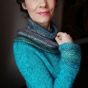 Może przedstawiać: Turkusowy sweter dzianinowy z wielokolorowym paskowanym golfem.