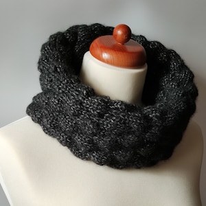 May include: A black knitted infinity scarf on a white mannequin. The scarf is made of a soft, textured yarn and has a simple, elegant design.