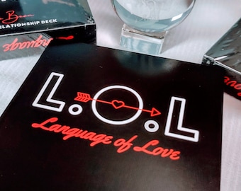 May include: A deck of cards with a black background and white lettering. The text on the front of the deck reads "L.O.L. Language of Love".