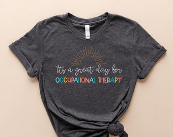 Pode incluir: Uma camiseta cinza escura com um gráfico de nascer do sol colorido e o texto "It's a great day for OCCUPATIONAL THERAPY".