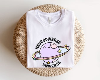 May include: White t-shirt with a graphic of a purple planet with a smiling face and the text "Neurodiverse Universe" in black.