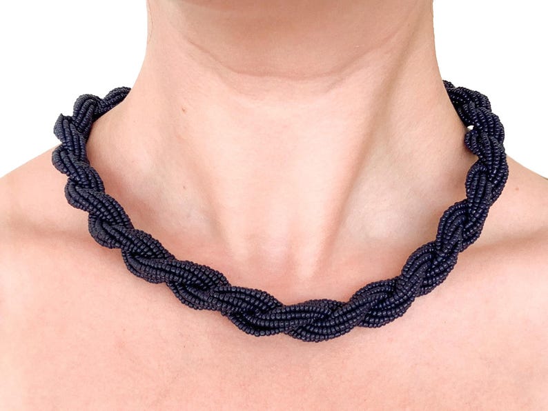 May include: A black beaded necklace with a twisted design. The necklace is made of small, round beads that are woven together to create a rope-like effect.