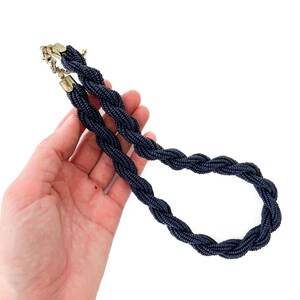 May include: A dark blue beaded necklace with a braided design. The necklace is made of small, round beads that are woven together to create a rope-like effect.