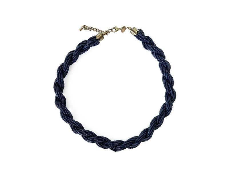 May include: A dark blue beaded necklace with a braided design. The necklace has a silver clasp.