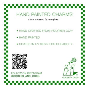 May include: White background with a green checkered border. Text reads "HAND PAINTED CHARMS" and "each charm is unique!". Bullet points describe the charms as hand crafted from polymer clay, hand painted, and coated in UV resin. Includes a QR code and Instagram handle.
