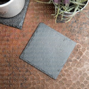 Peut inclure: Un dessous de verre en ardoise gris sur une surface de couleur cuivre. Le dessous de verre est carré et a une surface lisse légèrement texturée.