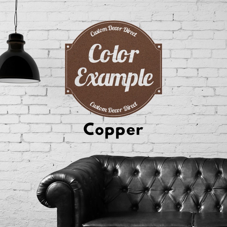 May include: A copper colored sign with the text "Custom Decor Direct" and "Color Example" on a white brick wall. The sign is above a black leather sofa.