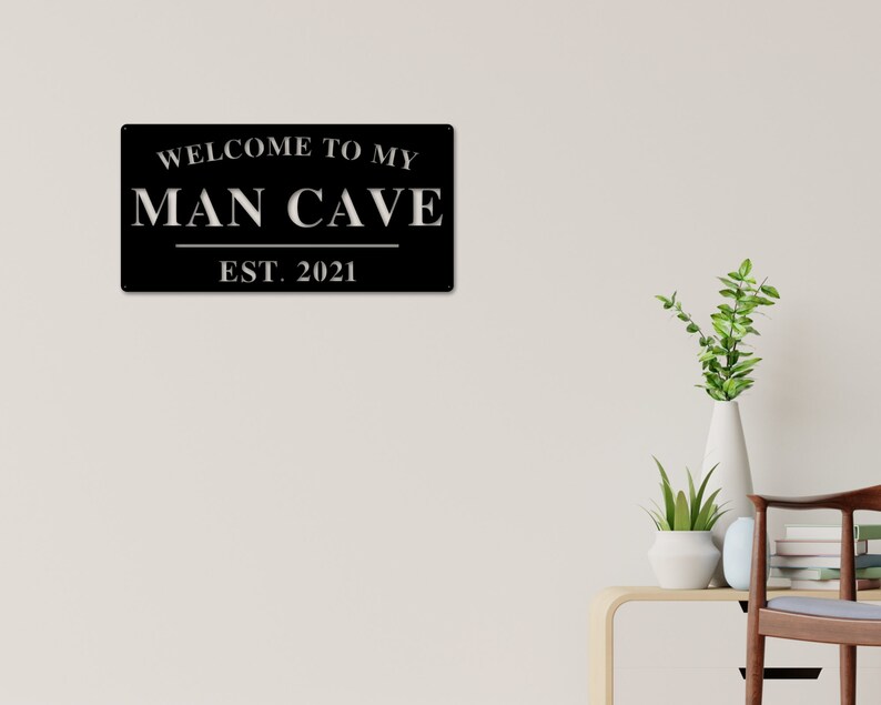 May include: Black metal sign with white text that reads "Welcome to my Man Cave Est. 2021".