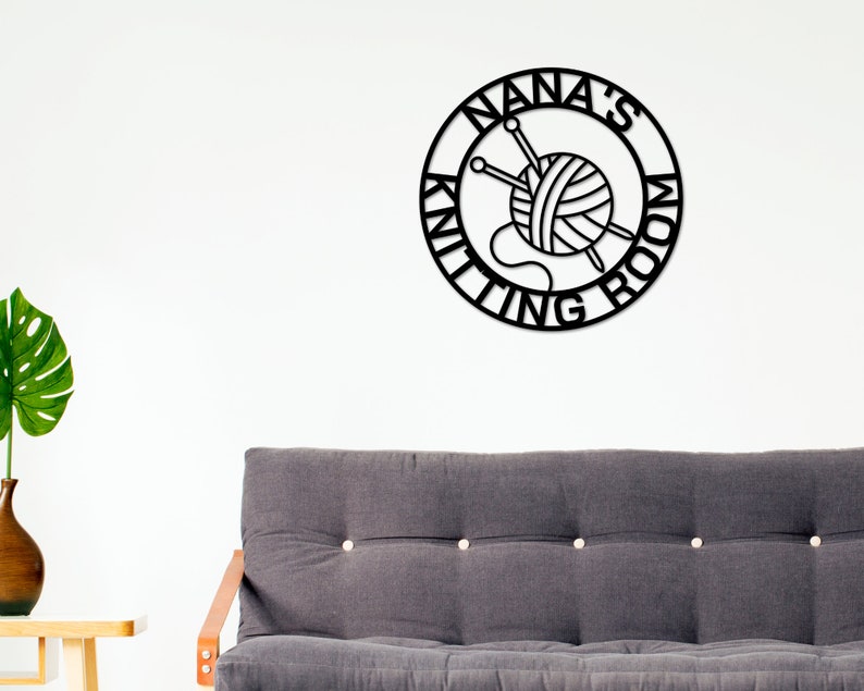 May include: Black metal sign with the text "Nana's Knitting Room" in a circle. The sign features a stylized image of a ball of yarn with knitting needles.