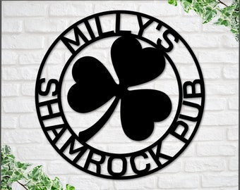 Puede incluir: Un letrero de metal negro con un diseño de trébol y el texto "Milly's Shamrock Pub".