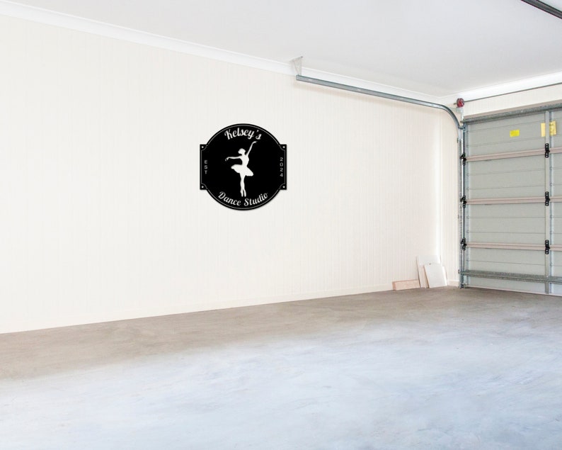 May include: A black and white sign with the text "Kelsey's Dance Studio" and a silhouette of a ballerina in a white dress. The sign is on a white wall in a garage.