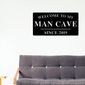 May include: Black metal sign with white text that reads "Welcome to my Man Cave Since 2019".