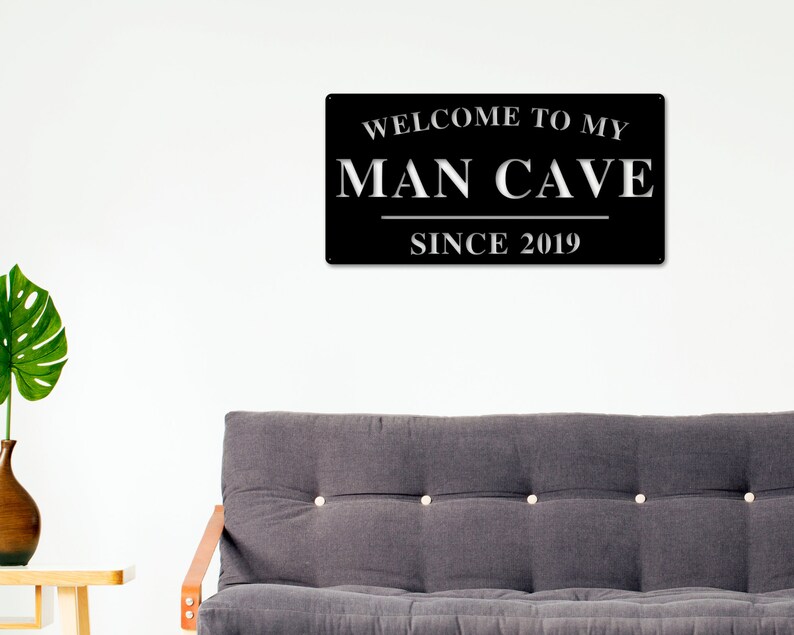 May include: Black metal sign with white text that reads "Welcome to my Man Cave Since 2019".