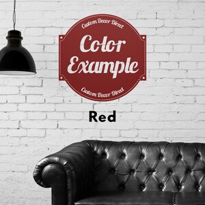 May include: A red circle sign with white text that reads "Custom Decor Direct" and "Color Example" with the word "Red" below the sign. The sign is on a white brick wall with a black leather couch in the foreground.