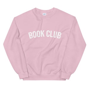May include: A pink sweatshirt with the text "BOOK CLUB" in white letters.