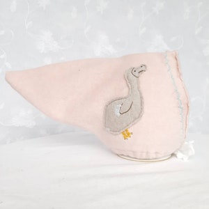 May include: A pink felt baby bonnet with a light blue trim and an embroidered gray bird design.