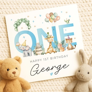 May include: A birthday card with the word "ONE" in light blue, decorated with cartoon animals, balloons, and a cake. The card reads "HAPPY 1ST BIRTHDAY George" in script. A teddy bear and a stuffed bunny are in the foreground.