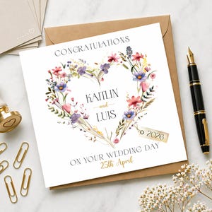 Puede incluir: Tarjeta de boda con diseño de corazón floral. La tarjeta dice "Felicidades" en la parte superior, con los nombres "Kaitlin and Luis" en el centro. También se muestra la fecha "25 de abril de 2026". La tarjeta está sobre un sobre marrón.